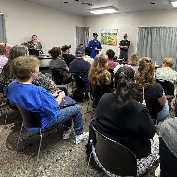 AT Instructor Alvin introduces a presenter in front of a room full of clients seated.